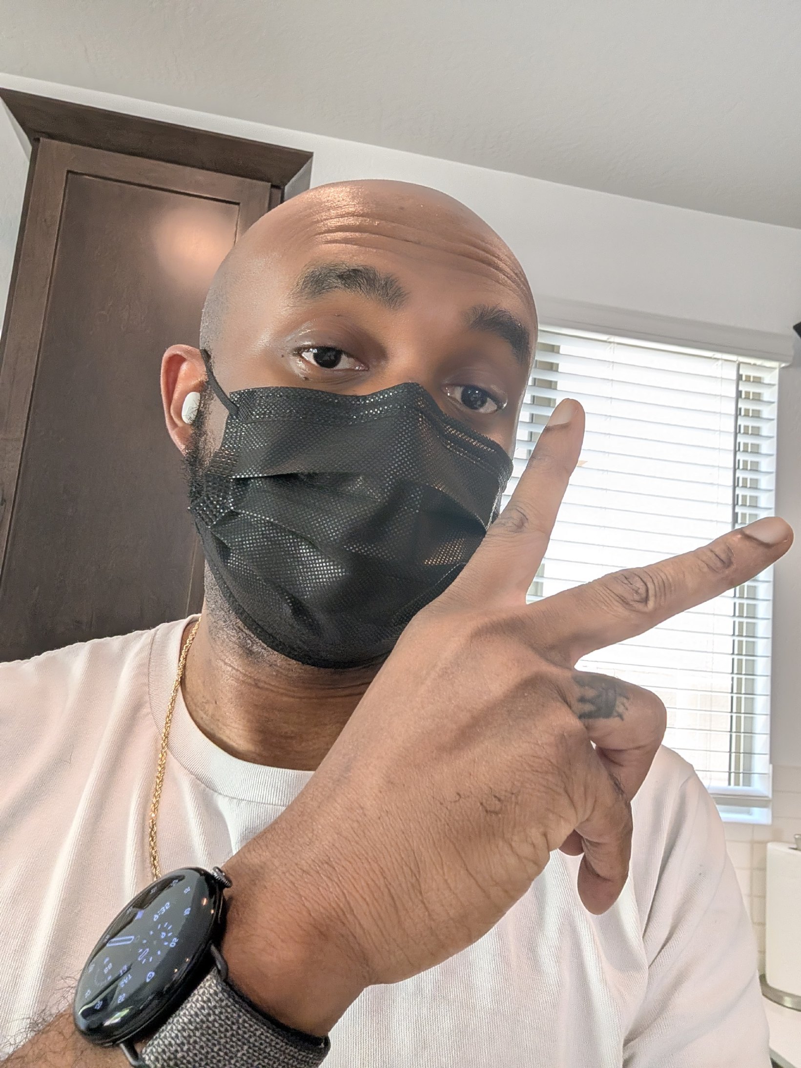 Me holding up a peace sign wearing a Pixel Watch 4 and wearing a mask