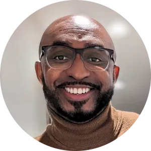 Michael Brown  wearing glasses and a brown turtleneck smiles warmly in a softly lit setting